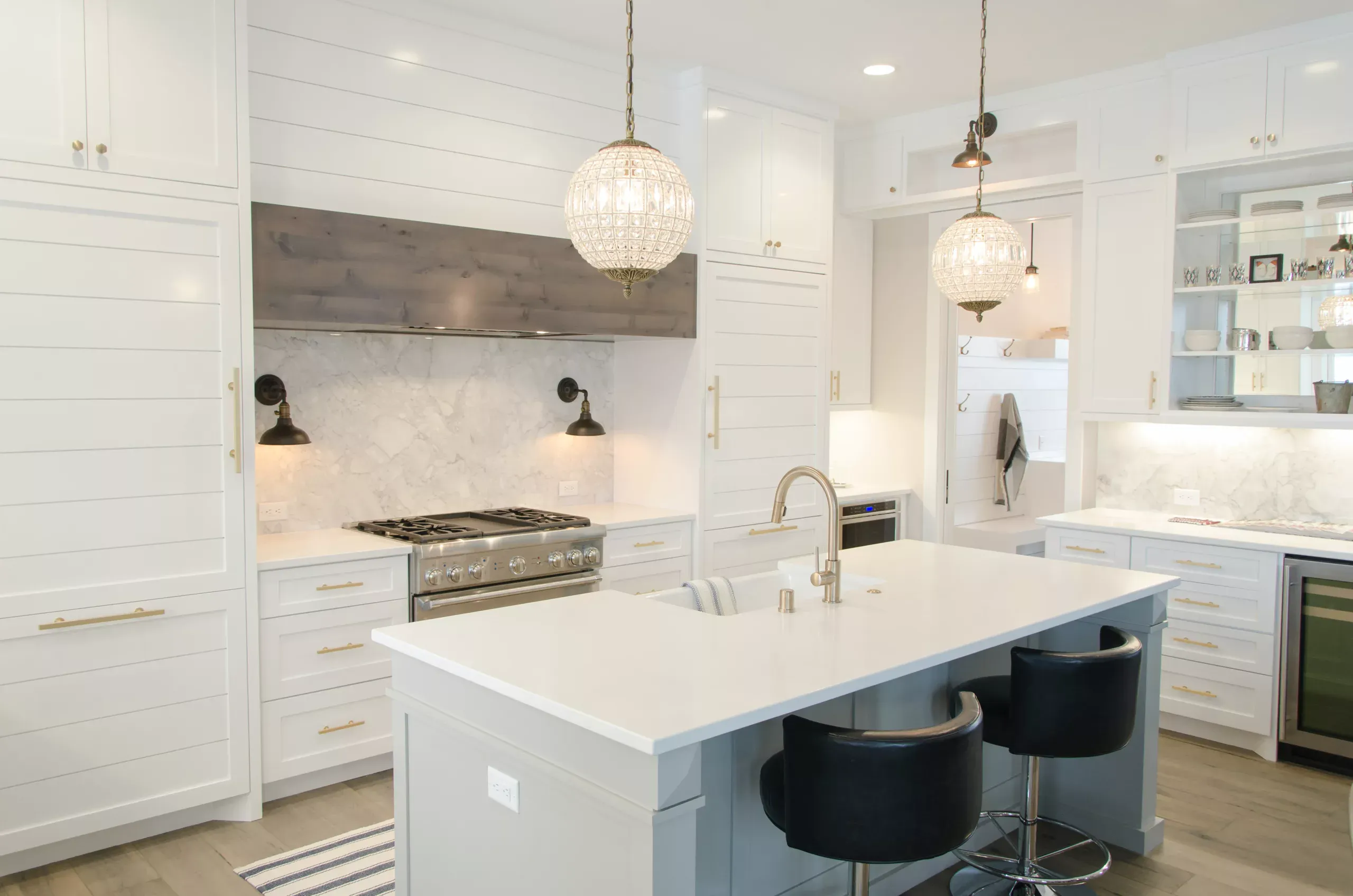 Bright white kitchen with shaker-style cabinetry, white quartz island with waterfall edge, black task chairs, stainless