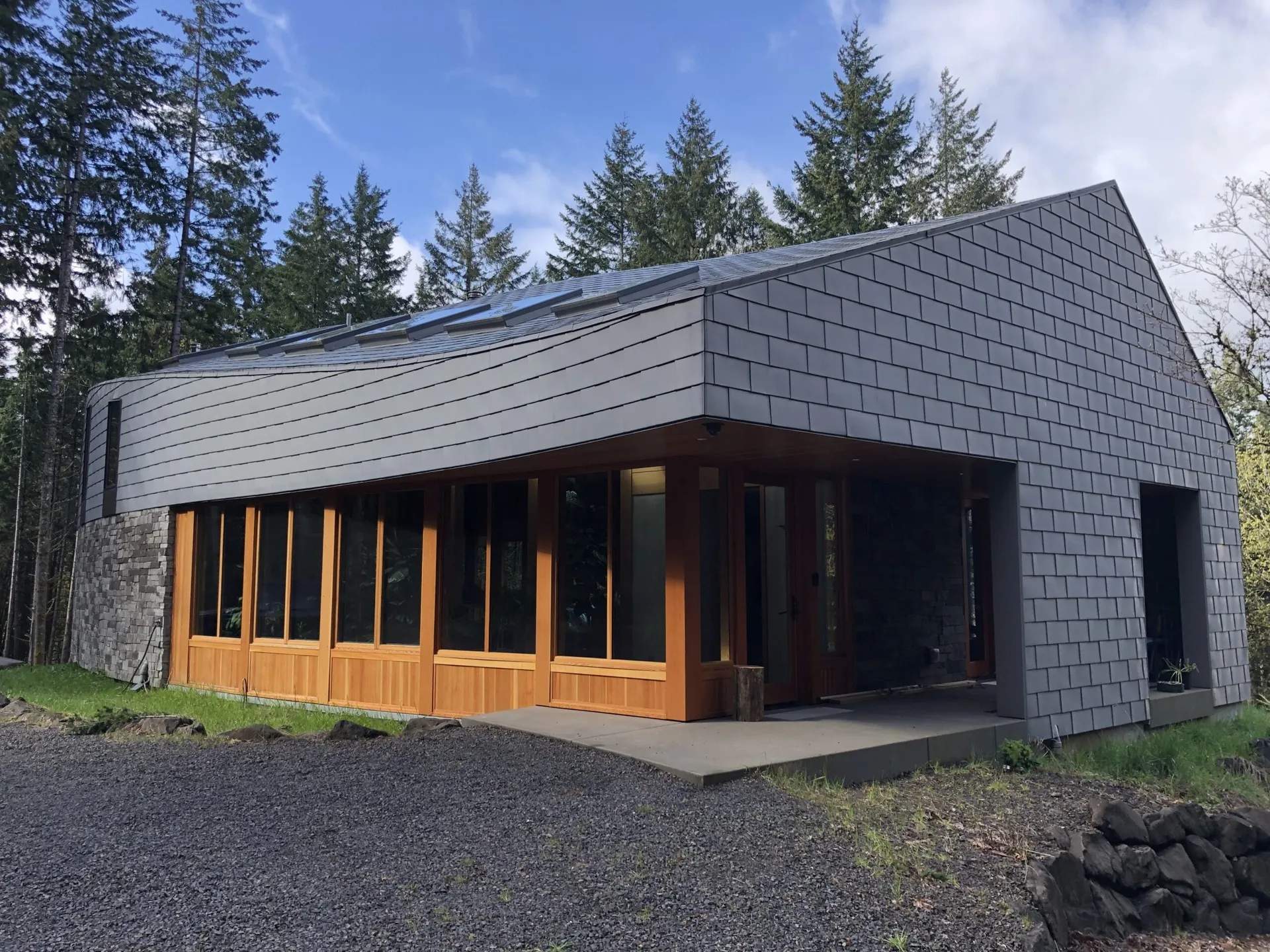 Contemporary home exterior featuring charcoal shingle siding, white metal soffit, wood-framed glass doors, and standing-seam
