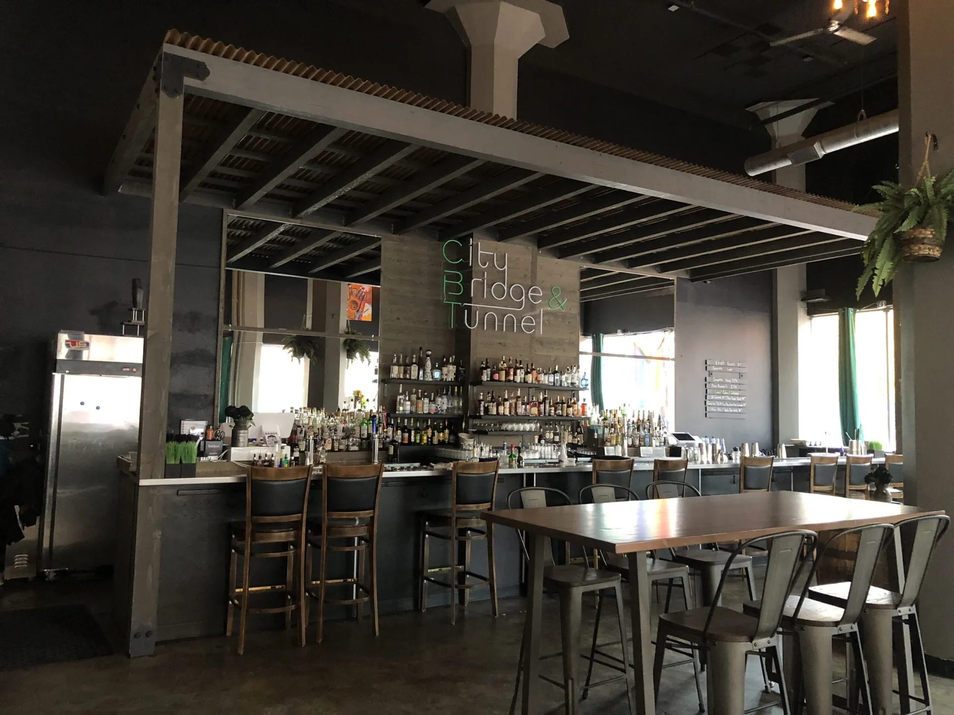 Modern bar restaurant interior with stainless steel service counter, wooden bar stools, exposed beam ceiling, and full