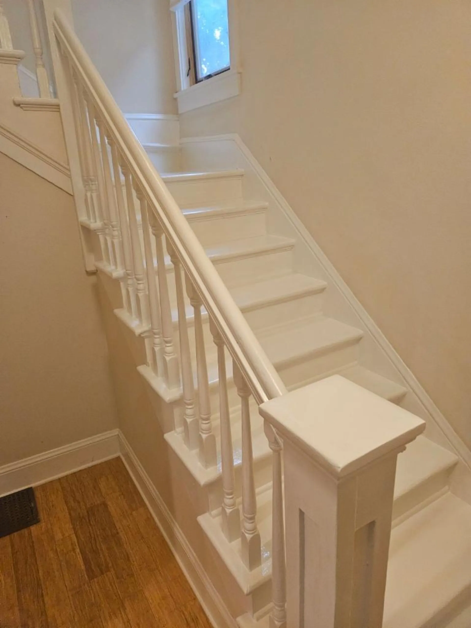 White painted interior staircase with spindle balustrade descending to wooden flooring, natural light from upper window.