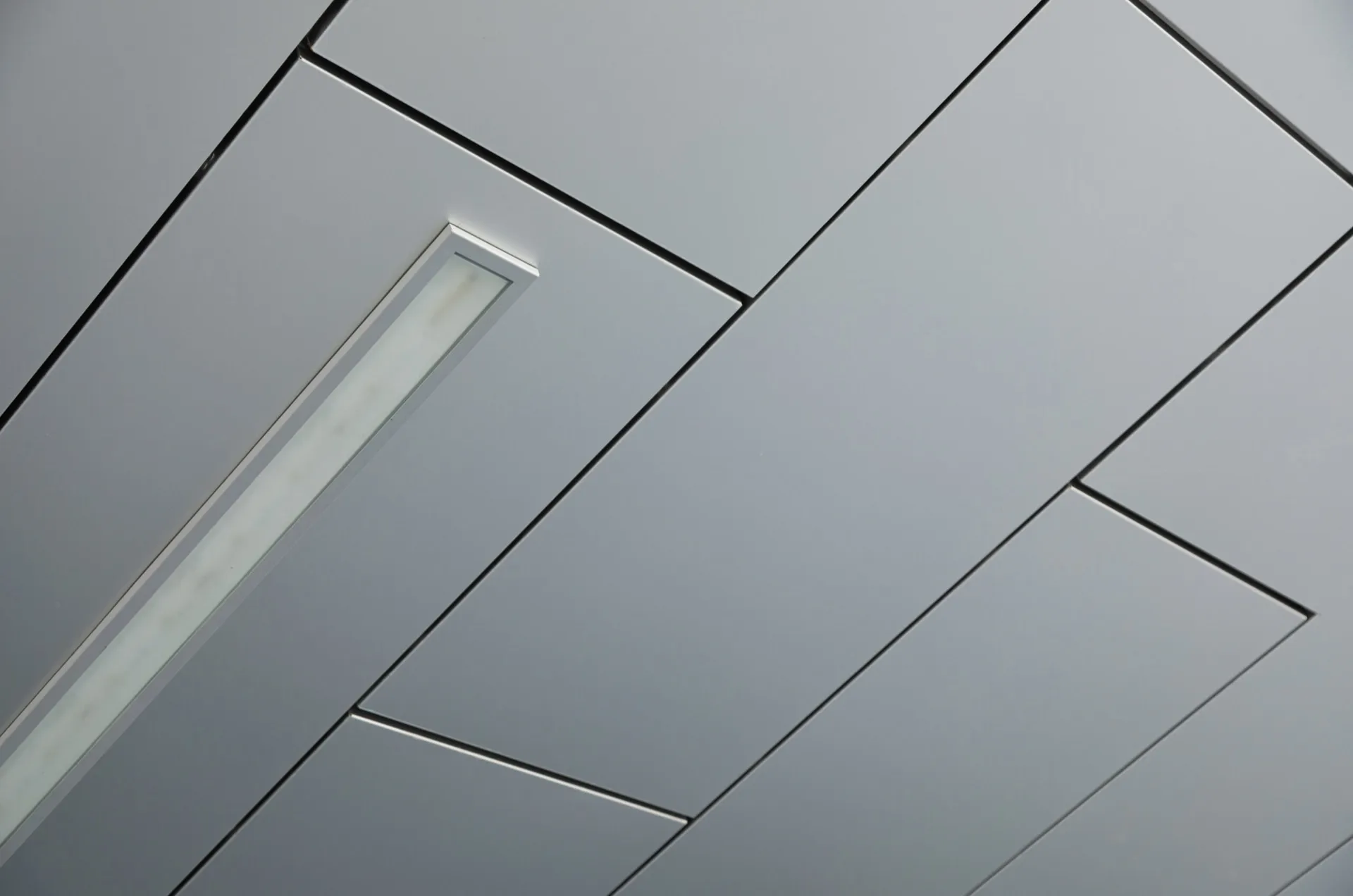 Suspended gray acoustic ceiling tiles arranged in a herringbone pattern with a white linear recessed light fixture running