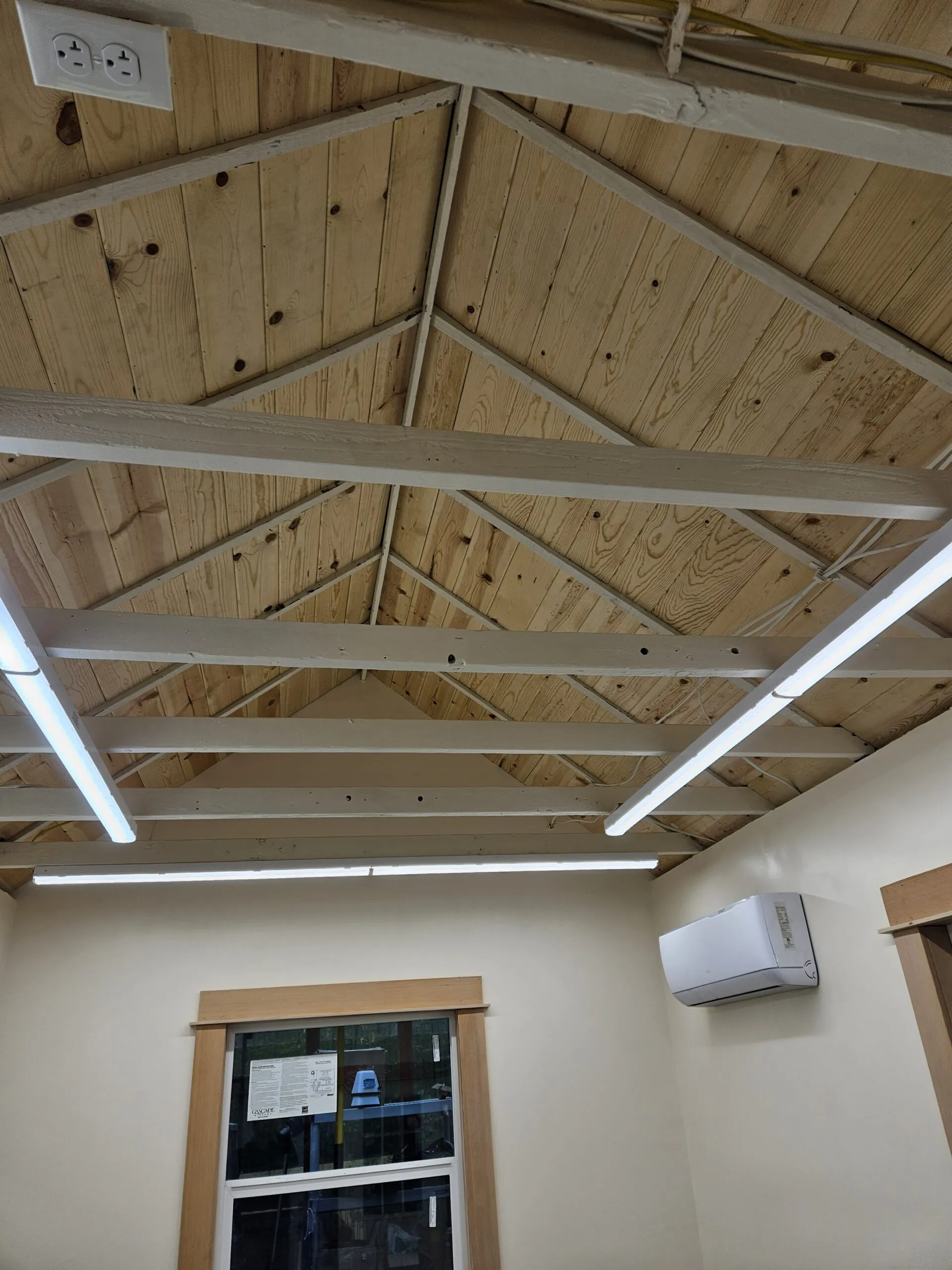 Vaulted wood beam ceiling with exposed framing, recessed LED light strips, and white ductless mini-split unit mounted on