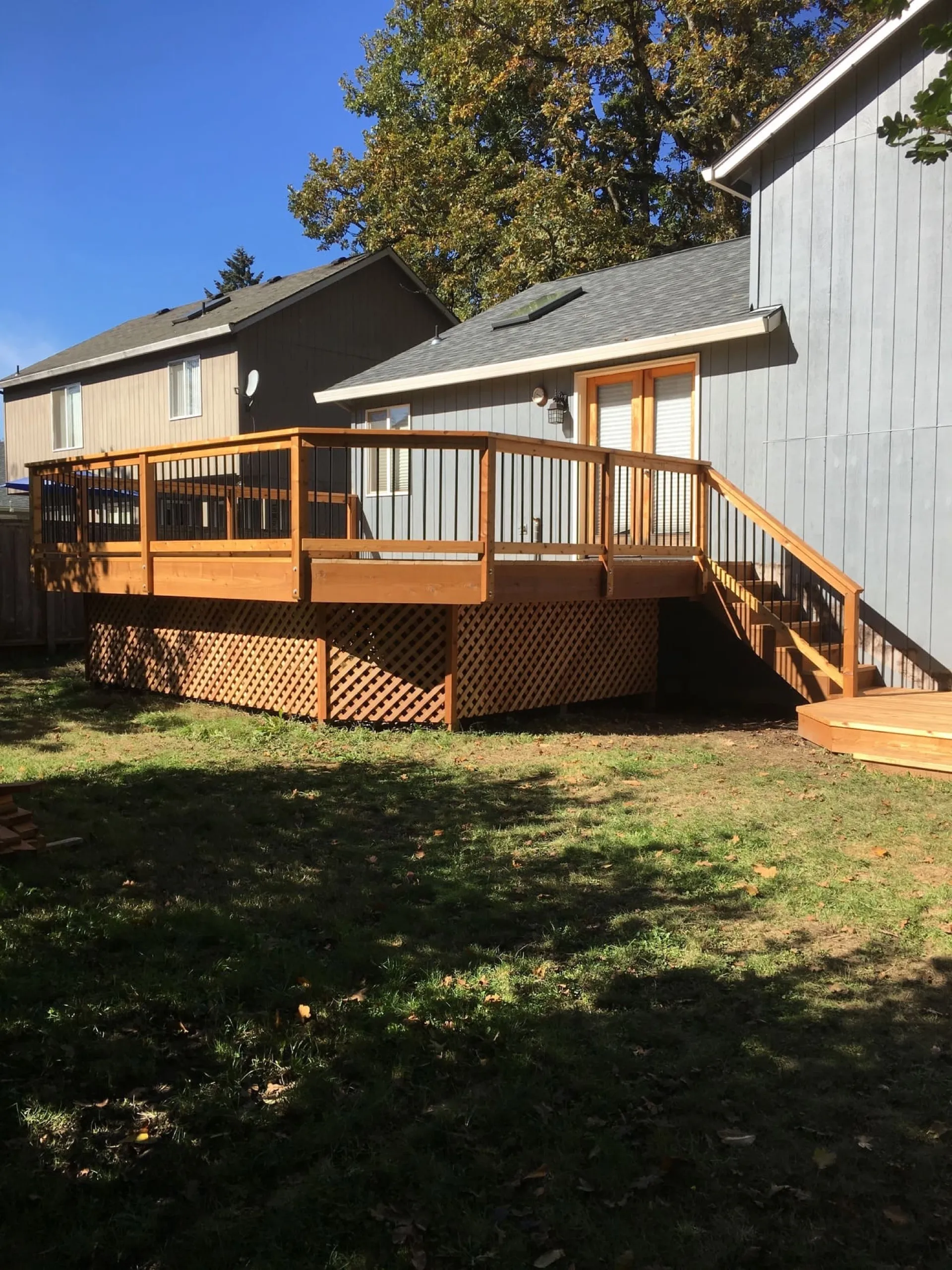 Multi-level wooden deck with tan railings, composite decking, and crosshatch lattice skirting attached to modern house with