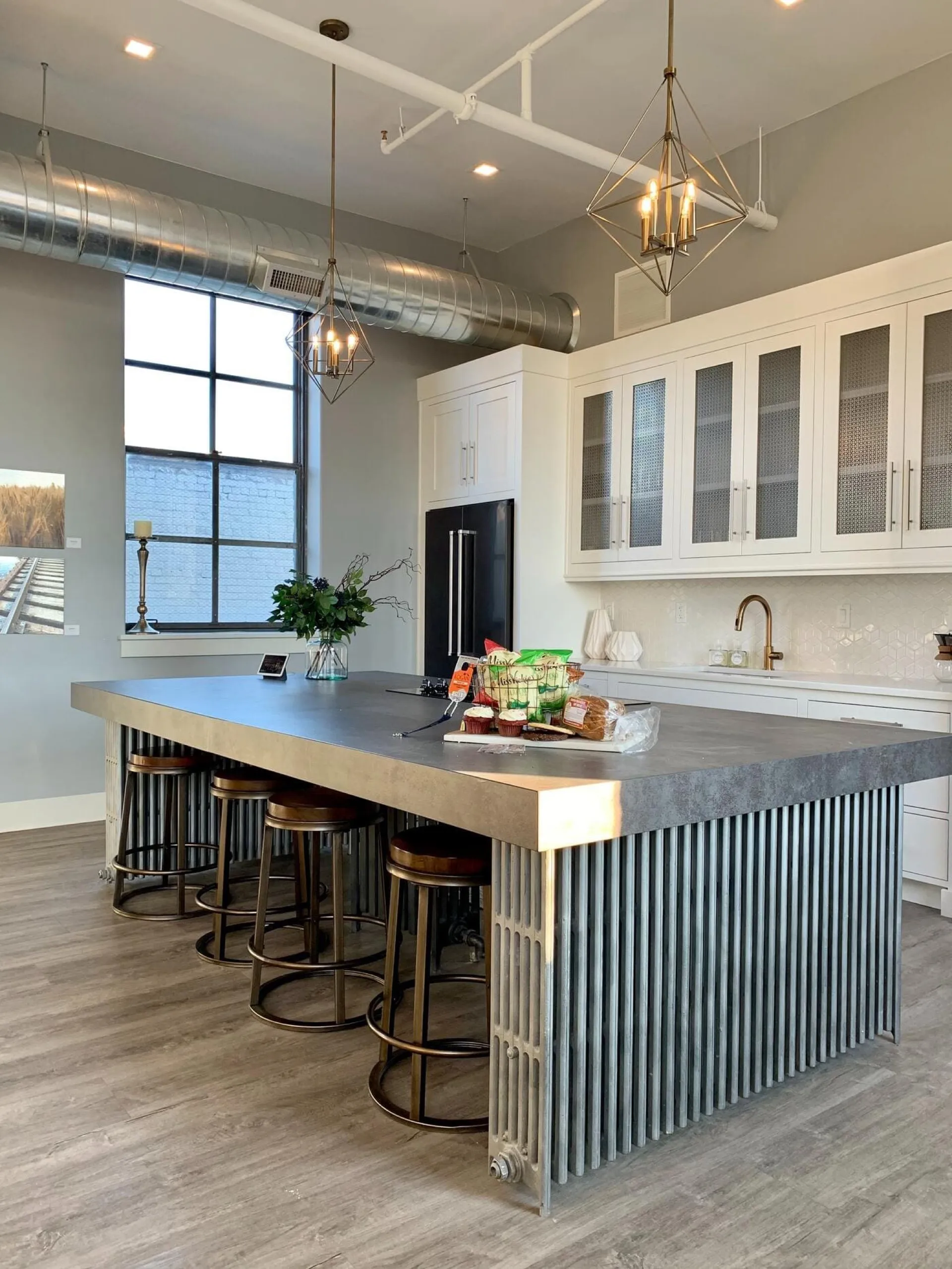 Modern kitchen with white upper cabinetry, gray lower island with wood countertop, three pendant lights, and large window
