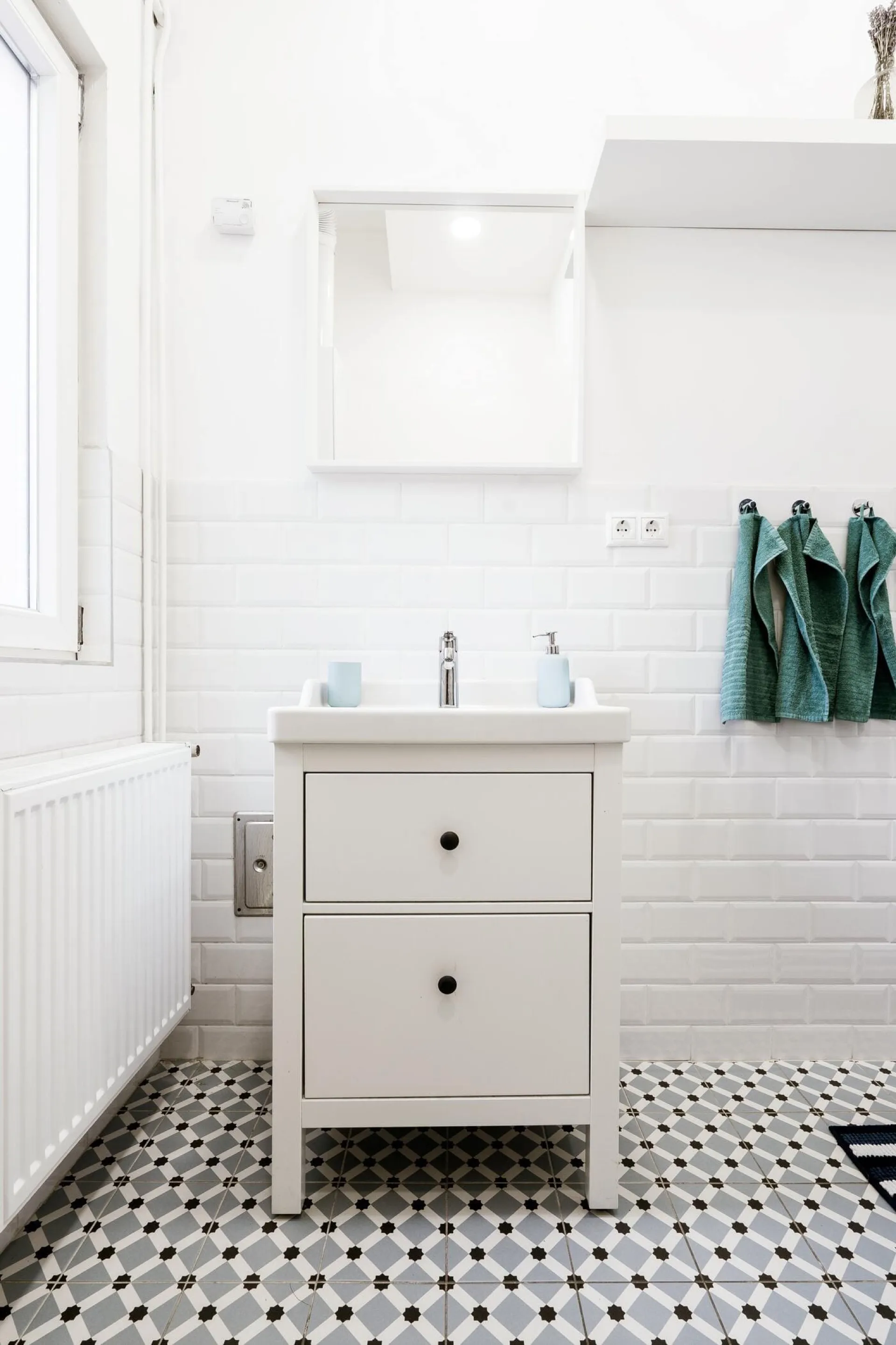 White wooden bathroom vanity with two black-knob drawers, white sink, and mirror above, set on black-and-white hexagonal