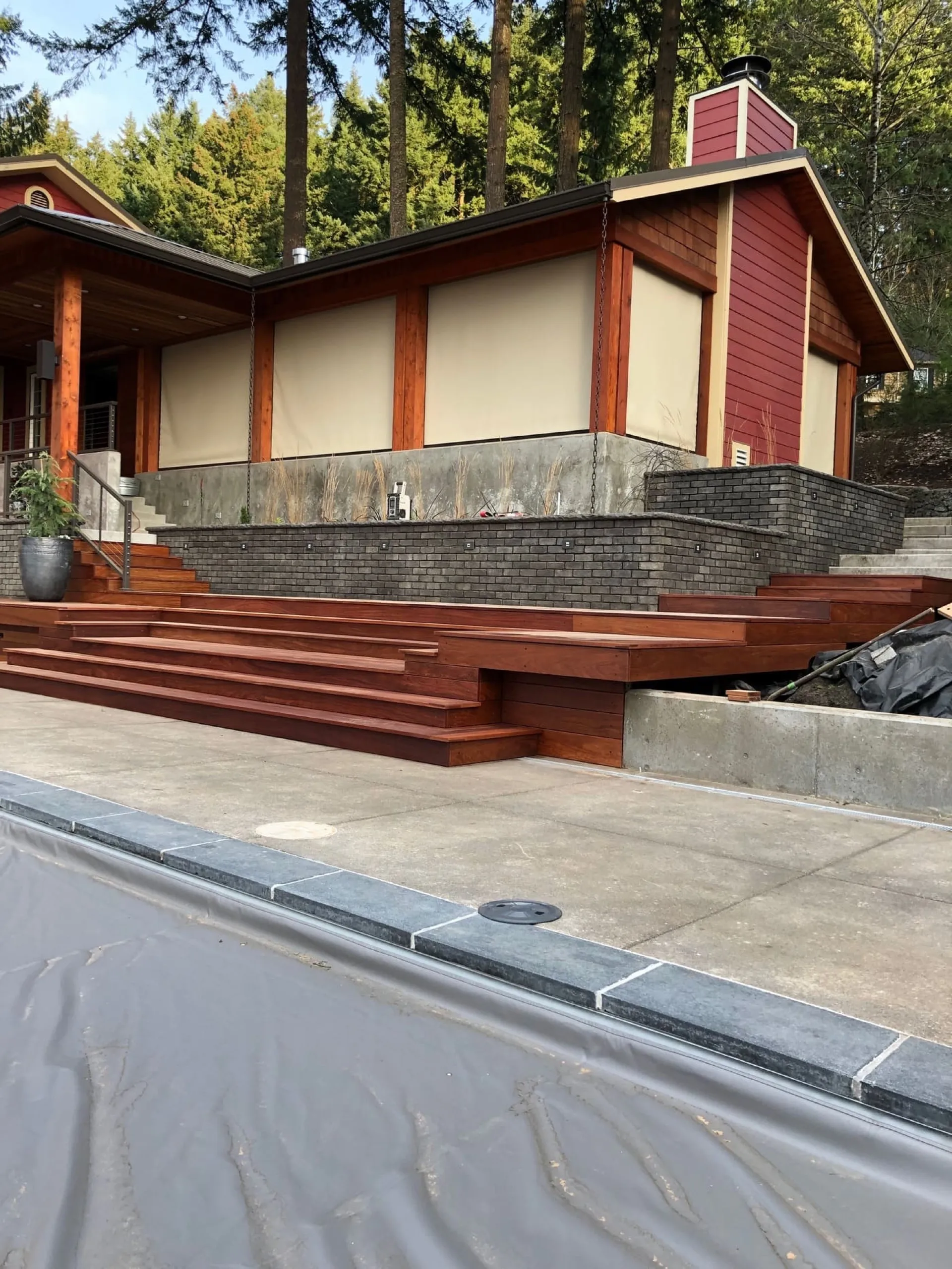 Modern home exterior with dark red vertical wood siding, cream stucco panels, horizontal mahogany-toned deck stairs