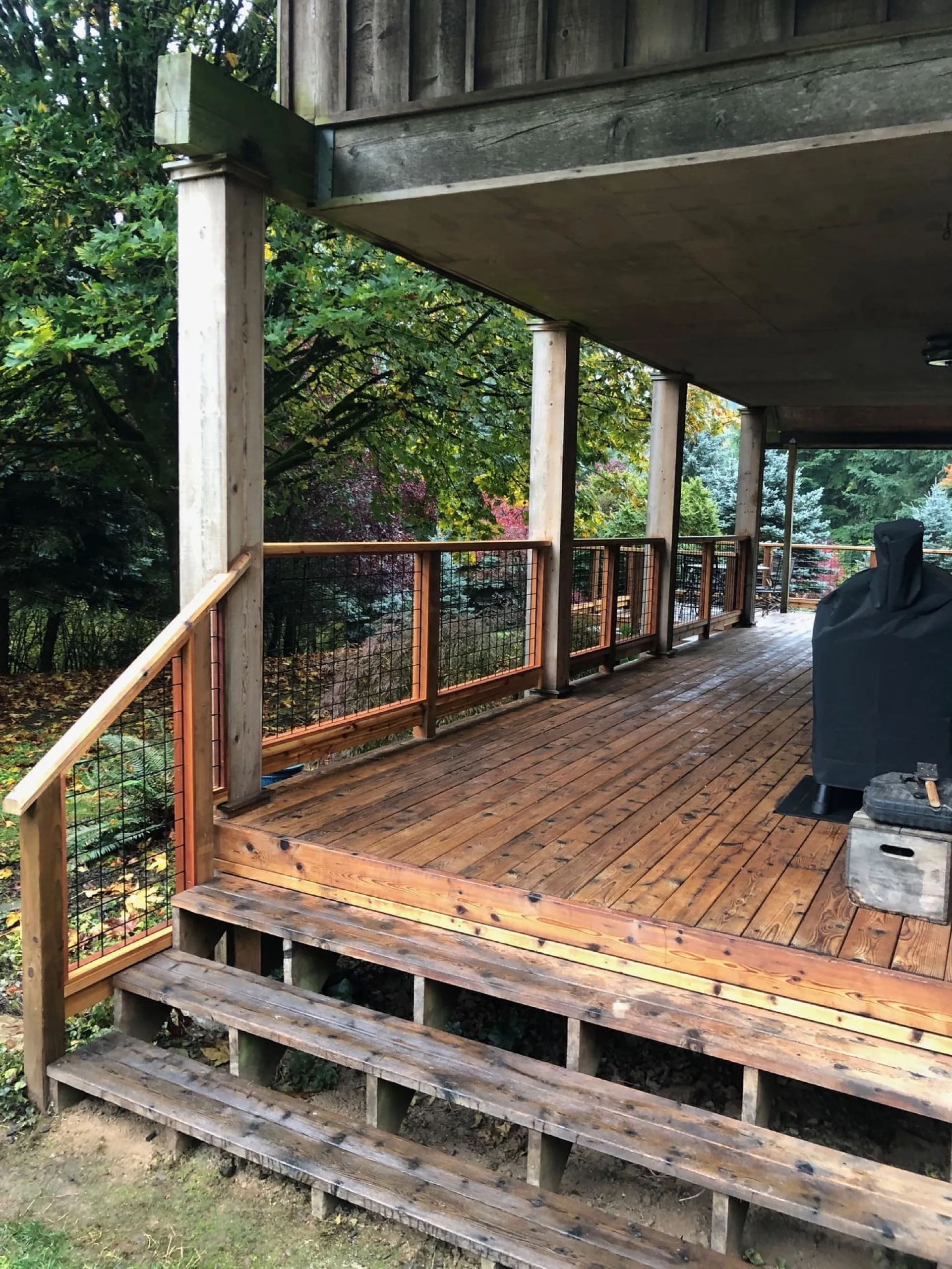 Wooden deck with composite boards, metal mesh railing, and concrete support structure overhead.