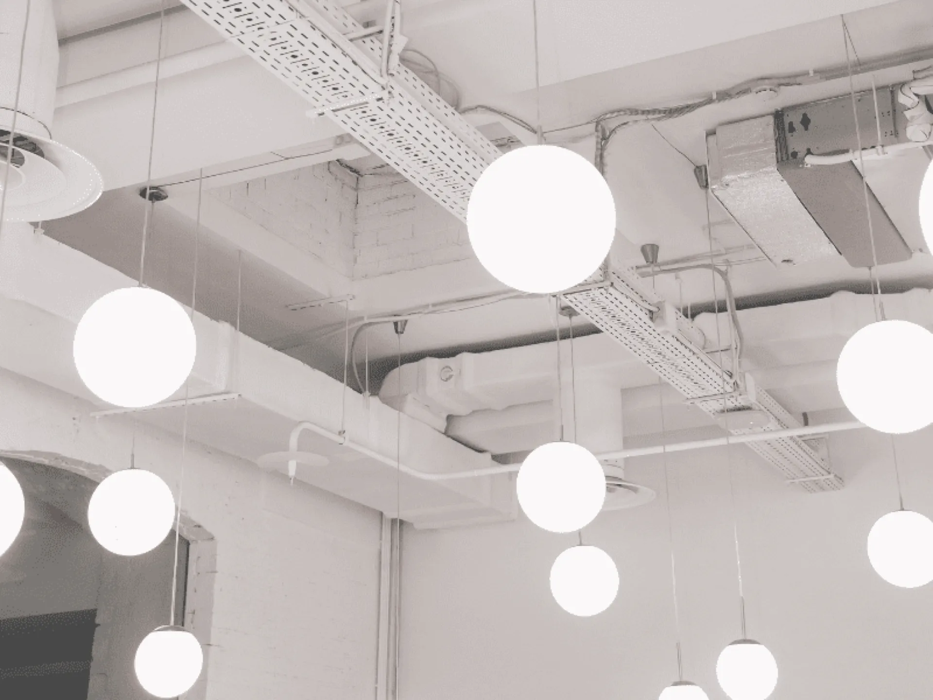 Multiple white globe pendant lights hang from a clean white ceiling with exposed metal ductwork and cable trays in a modern