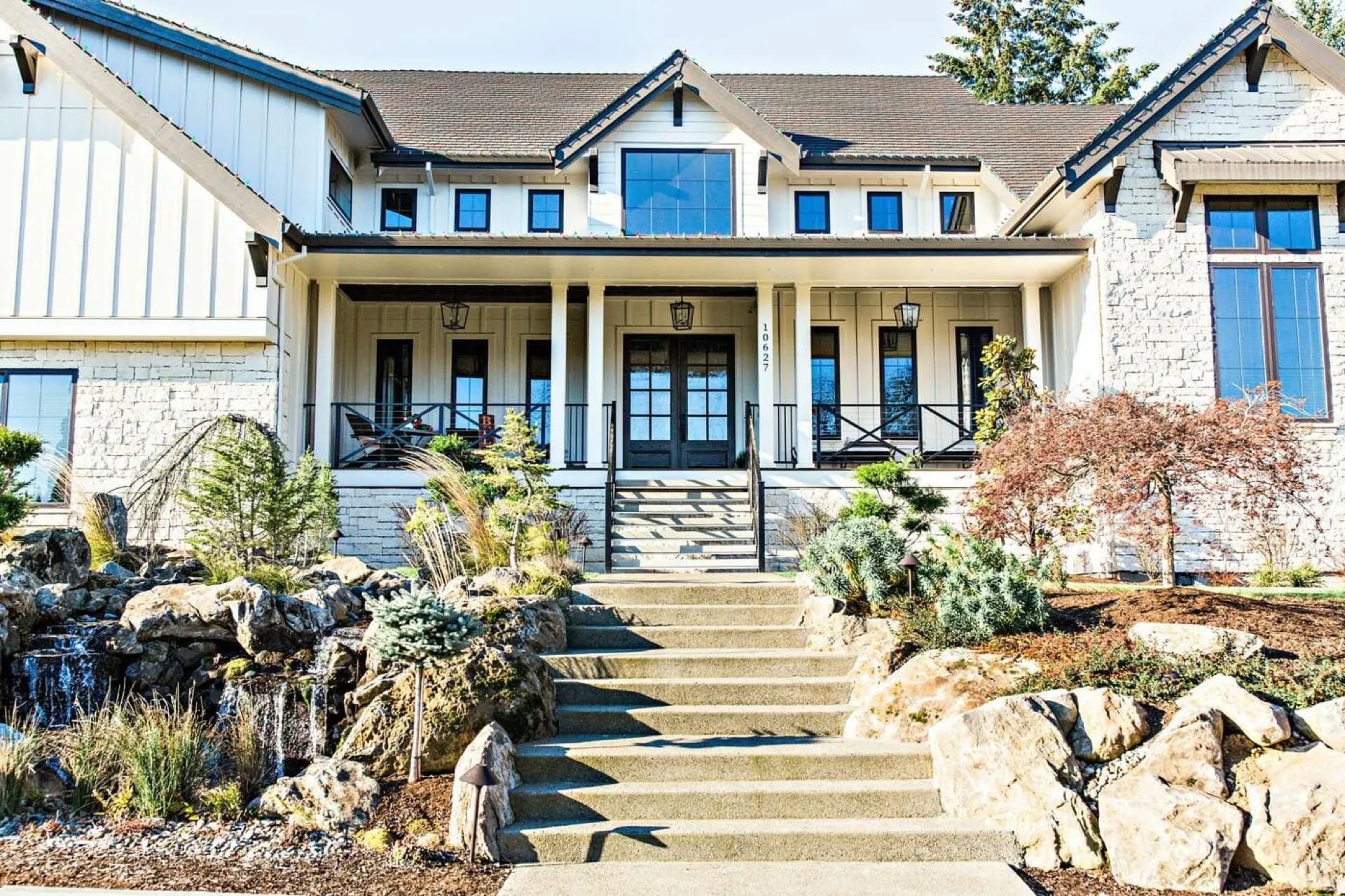 Modern farmhouse home with white columns, blue-shuttered upper story, stone and siding facade, covered front porch with