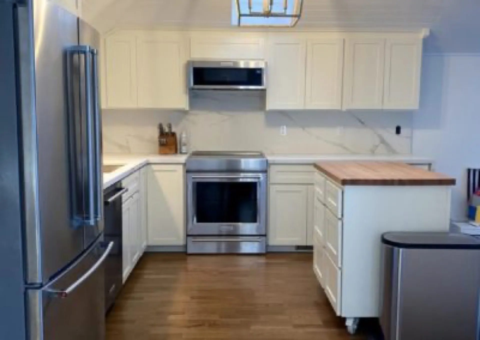 Modern kitchen with white shaker cabinetry, stainless steel refrigerator and range, marble backsplash, wood island